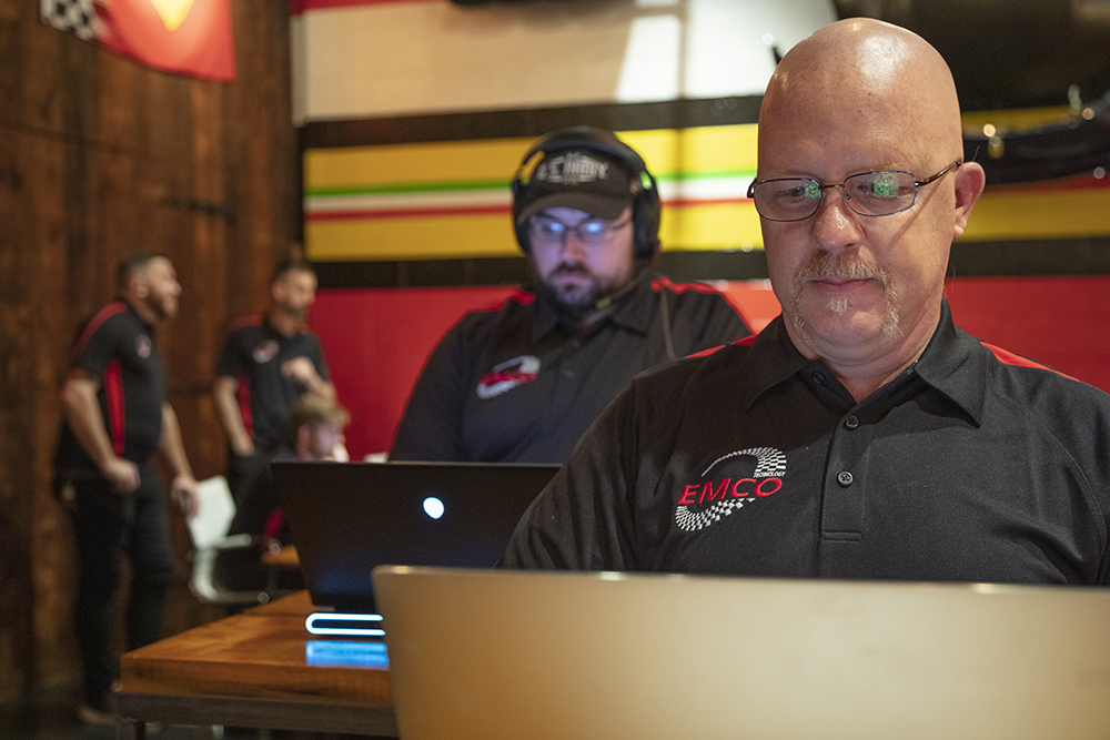 2 EMCO techs look at laptops. 2 other techs are in the background.