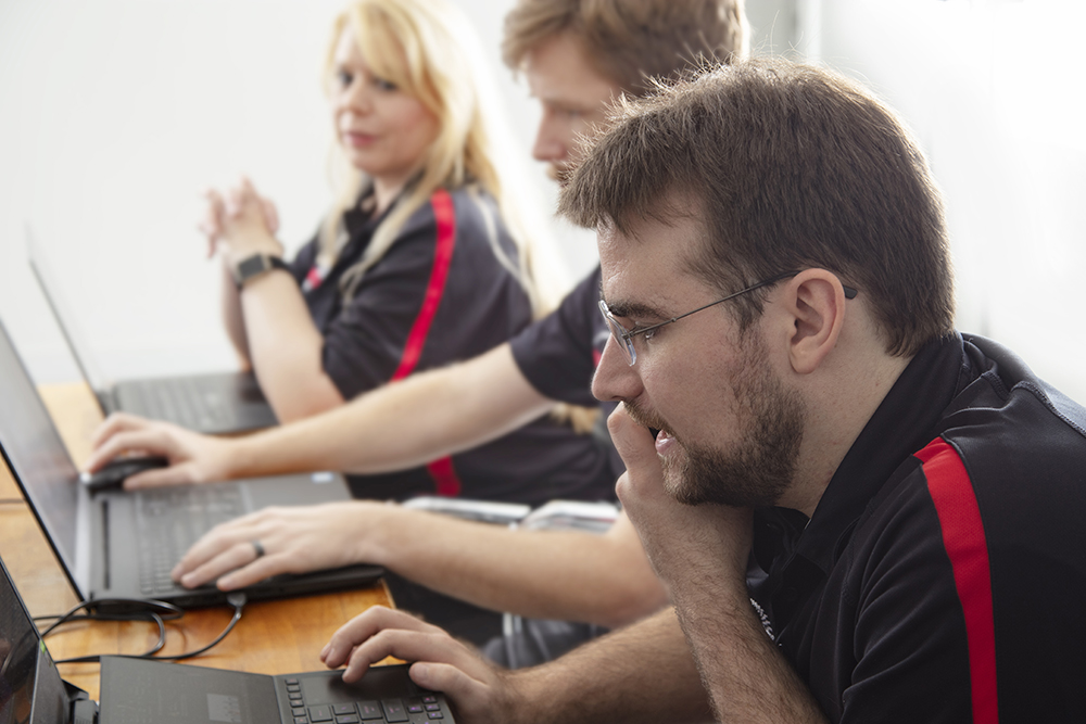 IT Outsourcing & Helpdesk image of 3 EMCO techs in black and red shirts look at laptops